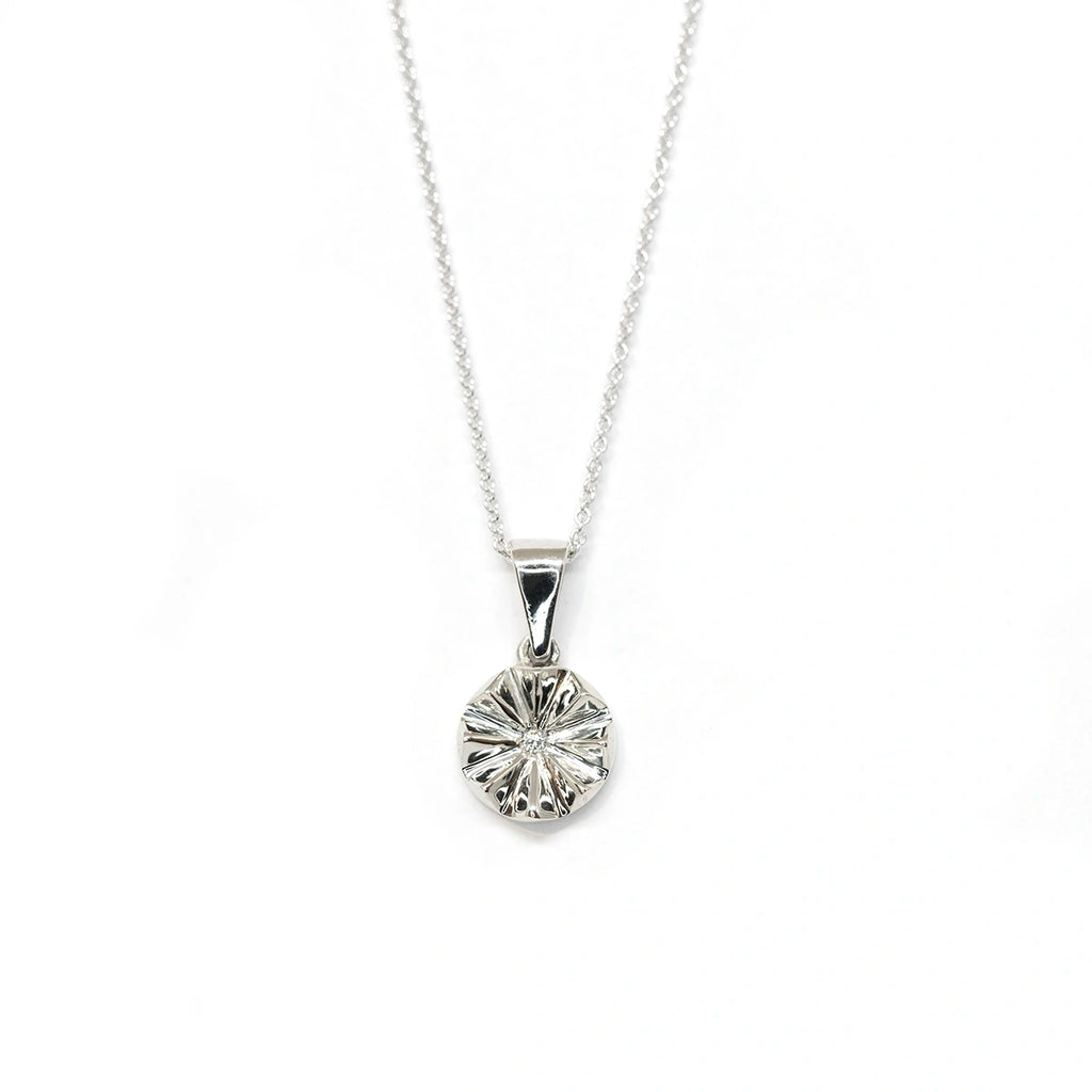 White gold round pendant with a central labgrown diamond seen on a white background. Fine jewelry made in Montreal by jewelry store Ruby Mardi for the Montreal CHUM Foundation.