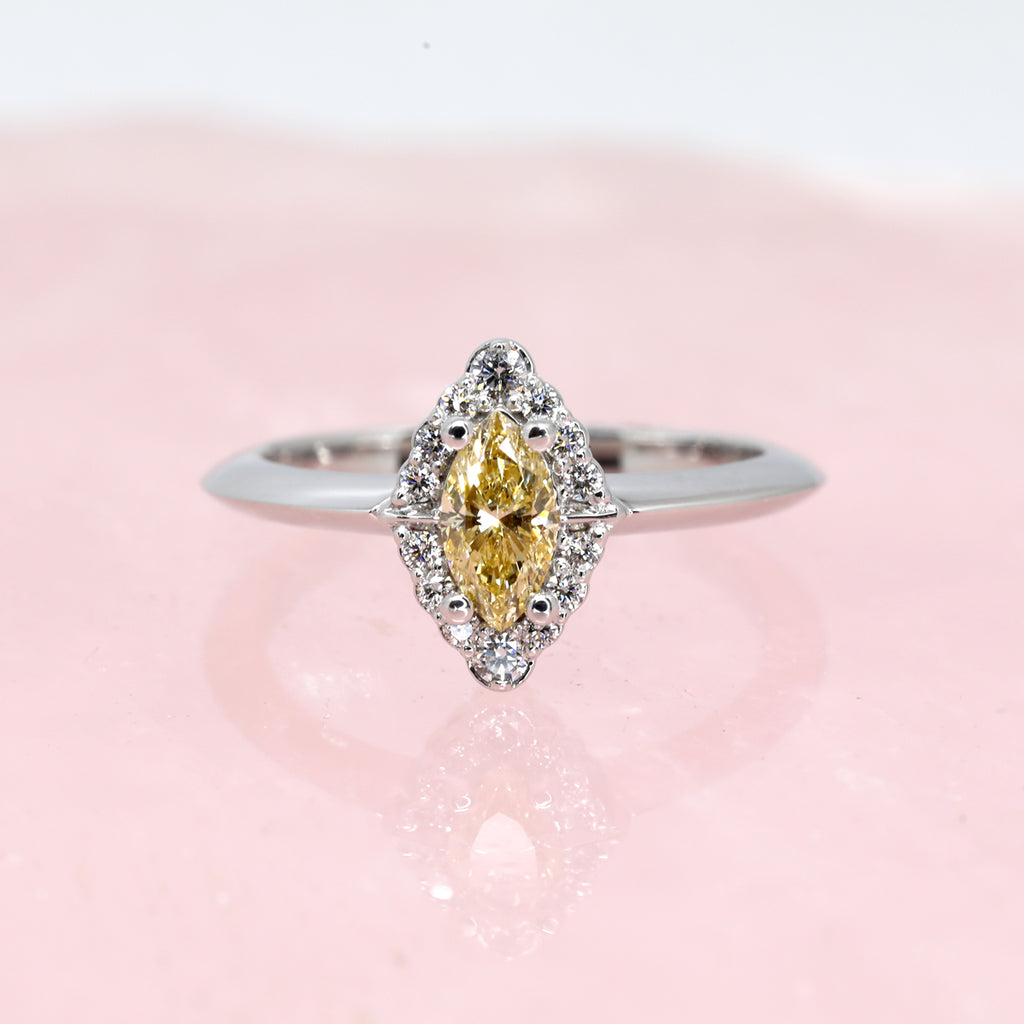 A classical engagement ring with a vintage touch featuring a big central yellow diamond and a diamond halo photographed on pink quartz. This bridal ring is available at fine jewelry store Ruby Mardi in Montreal’s Little Italy.