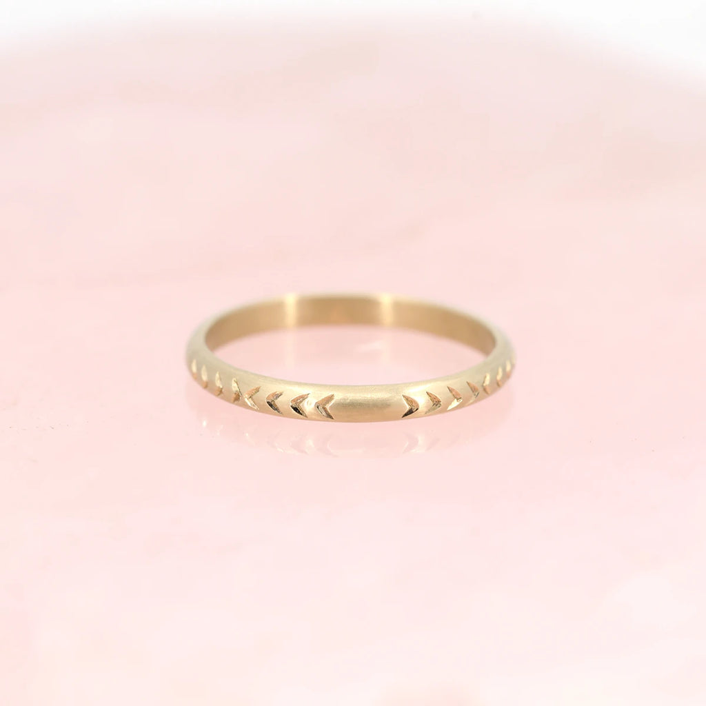 Organic gold band in 14k yellow gold with an hand engraved arrow pattern photographed over natural rose quartz. Alternative wedding jewelry available at fine jewelry store Ruby Mardi, in Montreal’s Little Italy.
