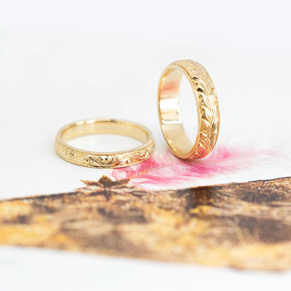 set of two rings in yellow gold engraved by hand men wedding band and  dainty engagement ring custom made in montreal by the jeweler boutique ruby mardi montreal on a multi color background