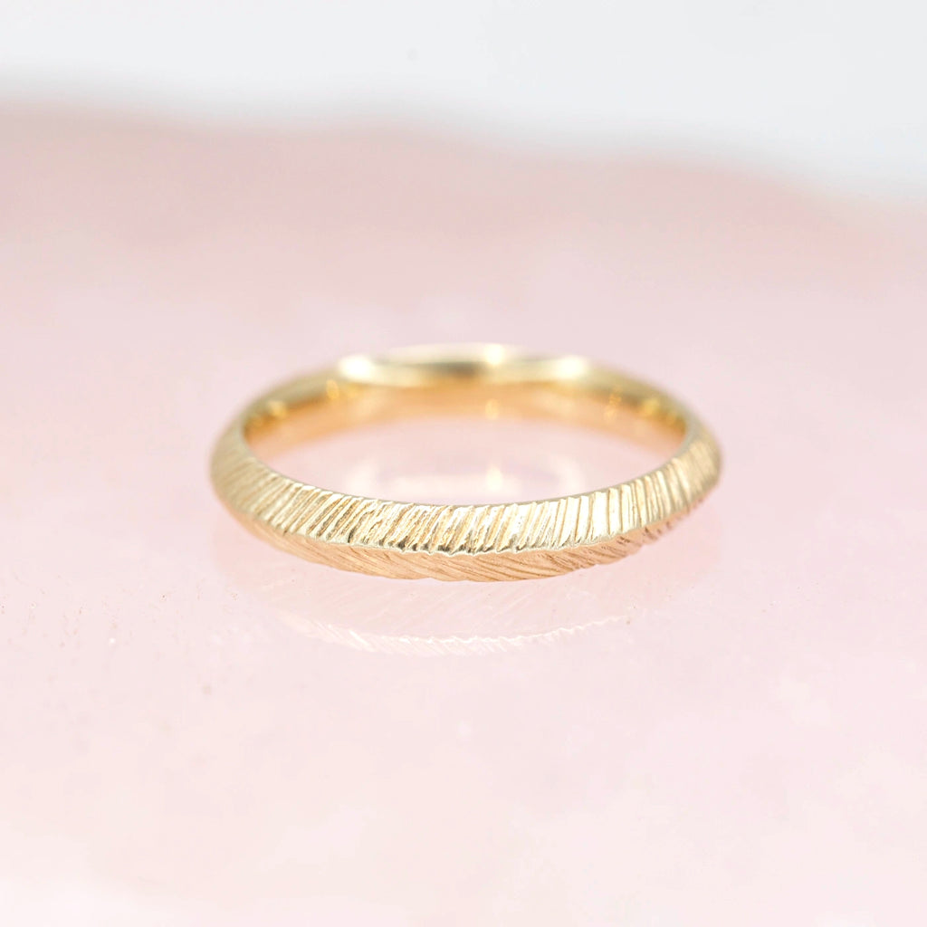 front view of yellow gold wedding band made by sheena montreal jewelry designer on a pink background