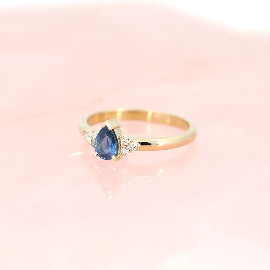 Blue sapphire engagement ring photographed on rose quartz and see from the side. One-of-a-kind bridal jewelry handmade in Canada and available at fine Jewelry store Ruby Mardi, in Montreal's Little Italy.