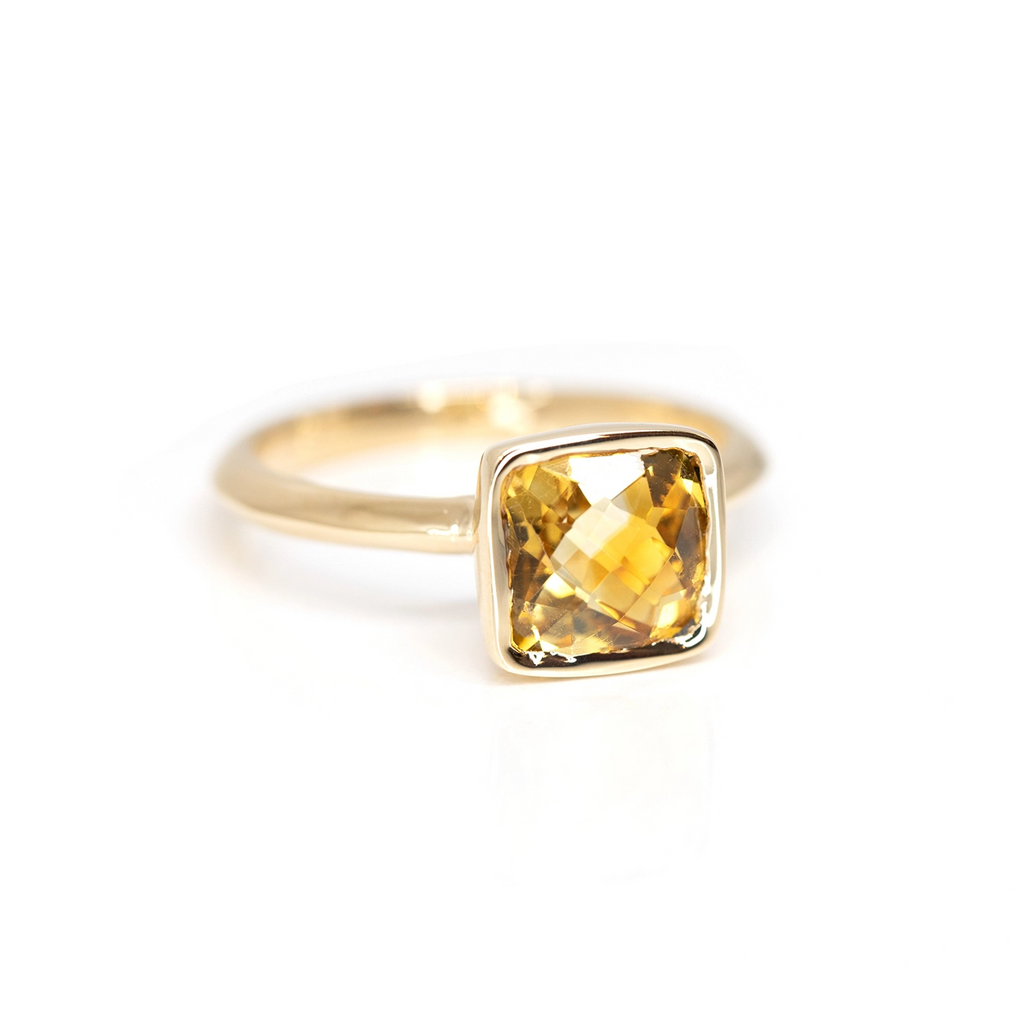 Half side view of a yellow gold ring with a bezel setting featuring a cushion cut citrine, seen on a white background. This ring was handmade and designed by Bena Jewelry in Montreal.