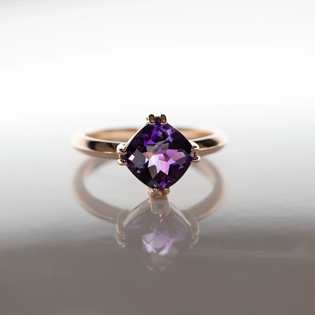 Front view of an amethyst rose gold ring featuring a deep purple high quality gemstone shown under a night light. 