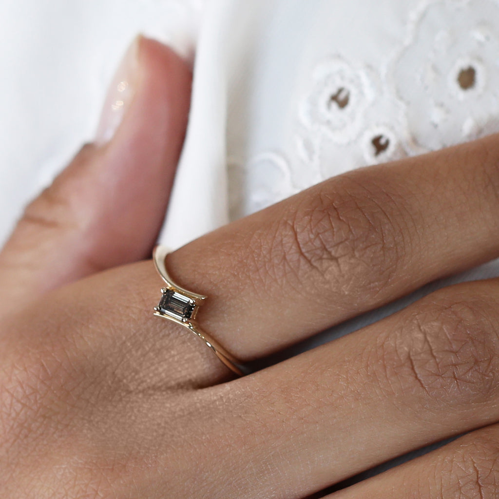 Close-up of a yellow gold engagement ring with an emerald-cut brown diamond worn on a hand, custom-made by Ruby Mardi in Montreal.