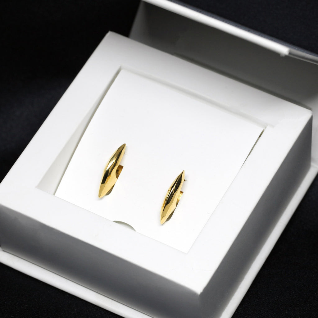 Pair of gold vermeil ALP earrings by Bena Jewelry displayed in a white jewelry box. These rough-faceted, statement hoop earrings feature an angular, sculptural design. Available at Ruby Mardi, a fine jewelry store in Montreal.