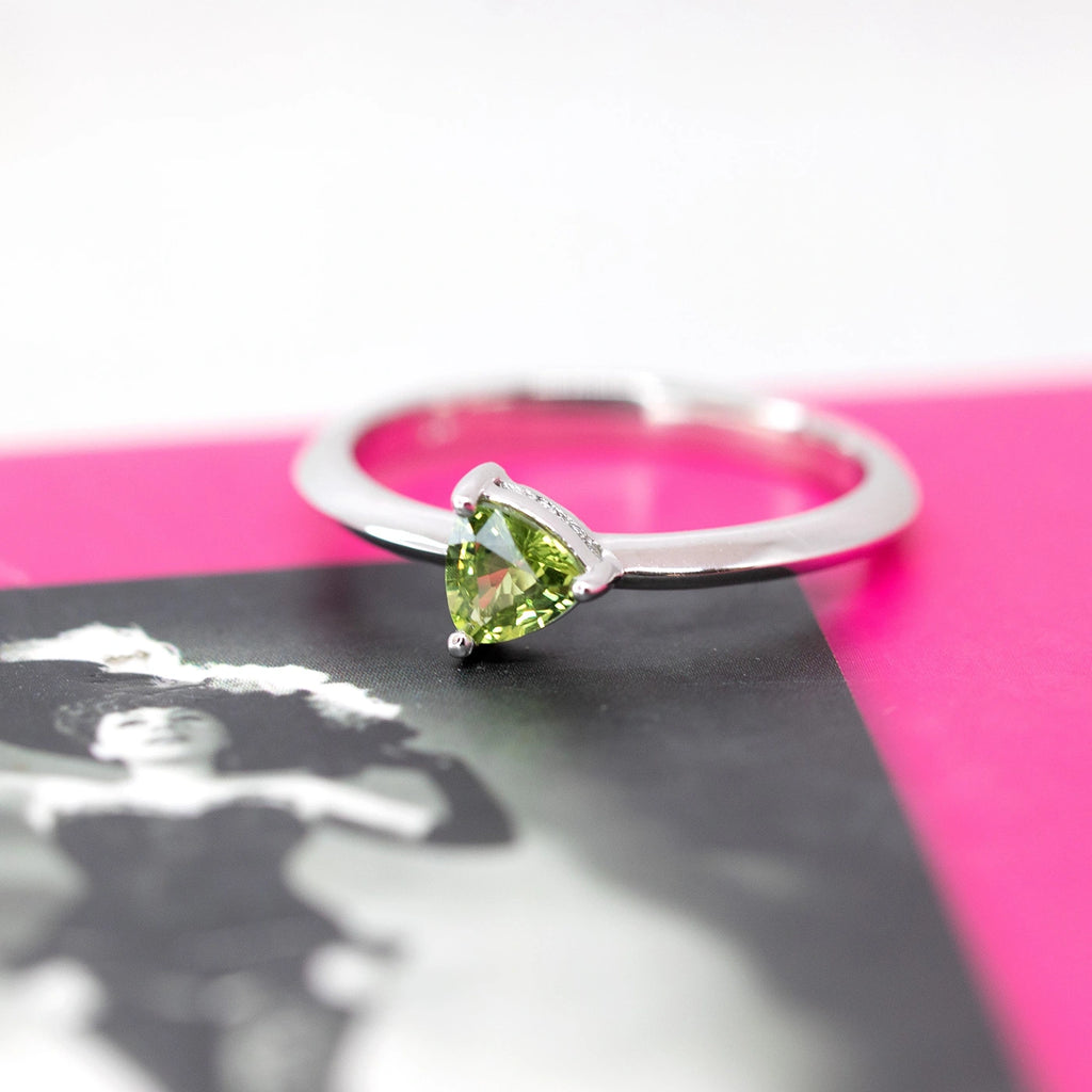 trillion shape green sapphire minimalist bridal ring in white gold custom made in canada by ruby mardi best fine jewelry store in montreal on a pink black and white background