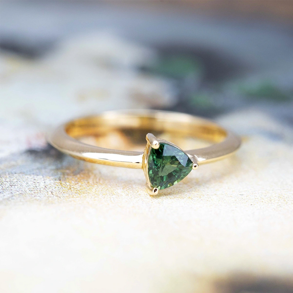 Front view of an engagement ring with a green color gem, natural sapphire, mounted on yellow gold. This splendid bridal ring is unique with a minimalist style, made in Montreal by the best jewelry store Ruby Mardi, specialist in fine jewelry from Canadian designers.