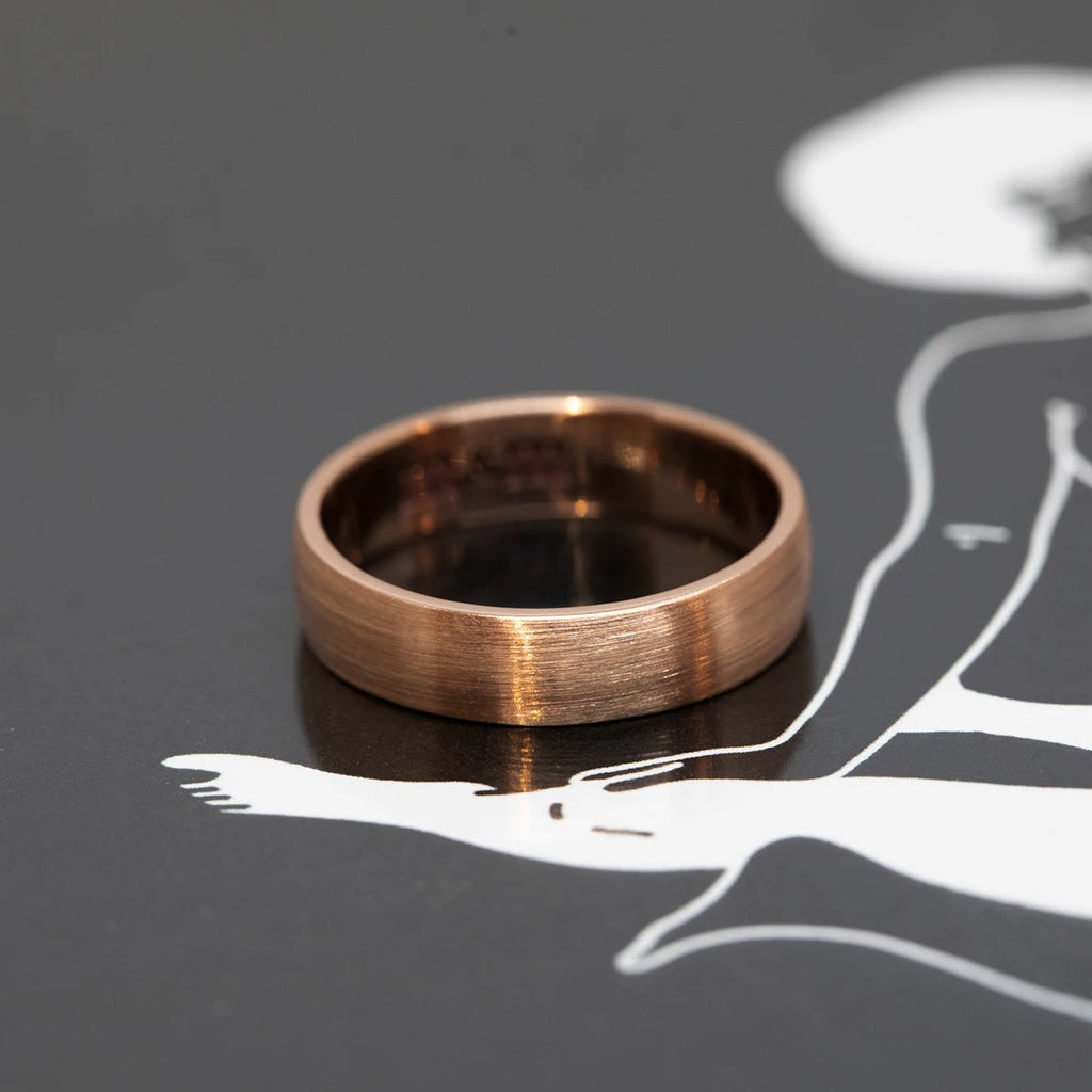 Men wedding band in rose gold with a mate finish custom handmade in Montreal and available at jewelry store RUBY MARDI. The wedding band is seen on a black background with white illustrations showing a couple in love. 