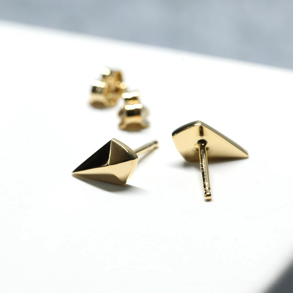Ruby Mardi yellow gold geometric studs resting on soft cream linen, emphasizing artisanal finish and minimalist style.