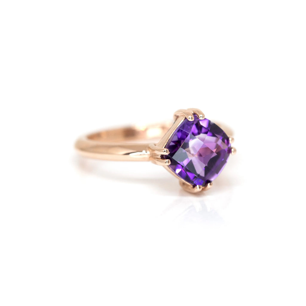 Half side view of a rose gold statement ring with a purple gemstone (a cushion cut amethsyt) handmade by fine jewellery designer Bena jewelry in Montreal, photographed on a white background.