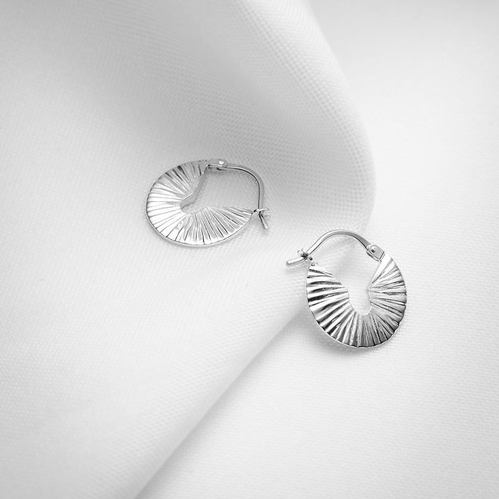 Small but chunky round textured sterling silver hoops handmade in Montreal by Veronique Roy JWLS photographed on a white fabric. Available at jewelry store Ruby Mardi, in Little Italy.