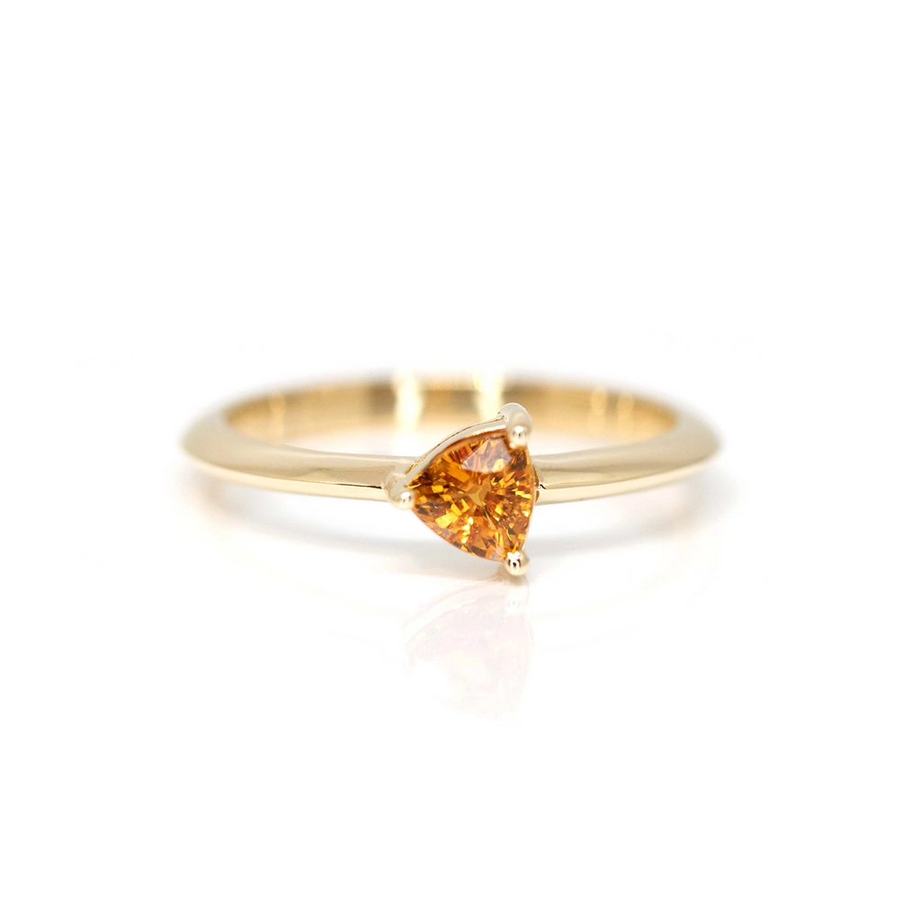 Orange sapphire yellow gold bridal ring in a trillion shape custom made in Montreal by designer Bena Jewelry, seen on a white background.