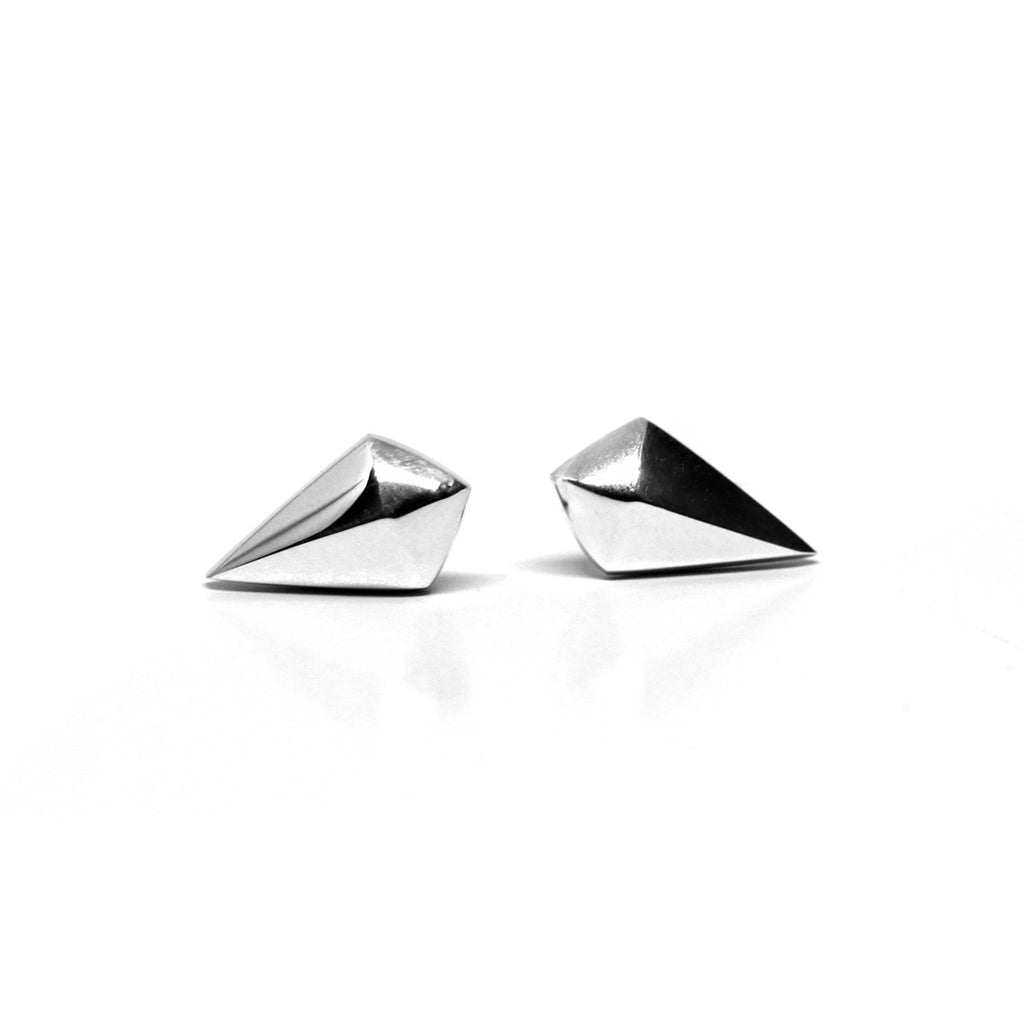 Ruby Mardi present a close-up of single pointed gold earring by Bena Jewelry, showcasing its reflective finish on a white surface.