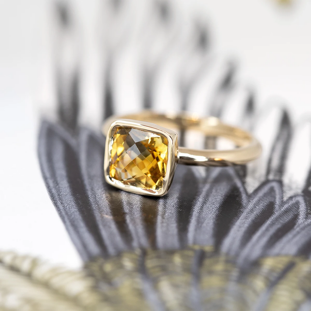 Side view of a yellow gold one of a kind statement ring handmade in Montreal by local brand Bena Jewelry featuring a cushion cut citrine. The ring is seen on an abstract background.