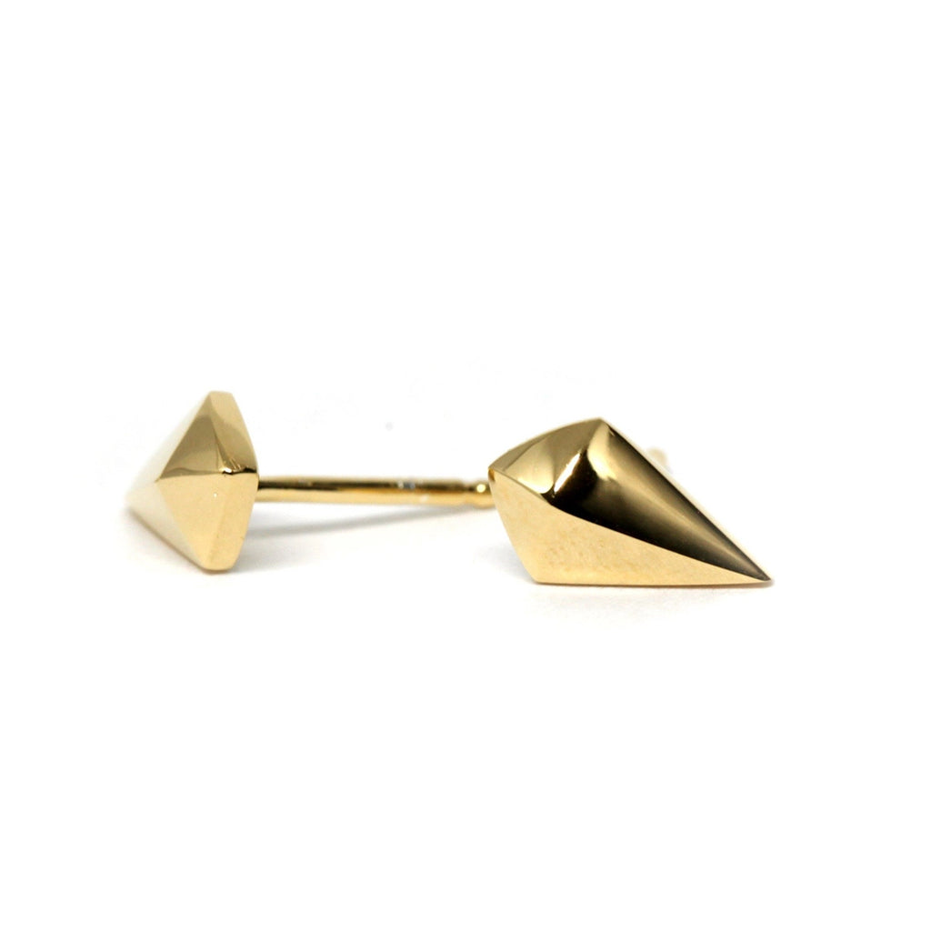 Angular stud earrings in yellow gold placed on pale wood surface, with soft natural lighting.