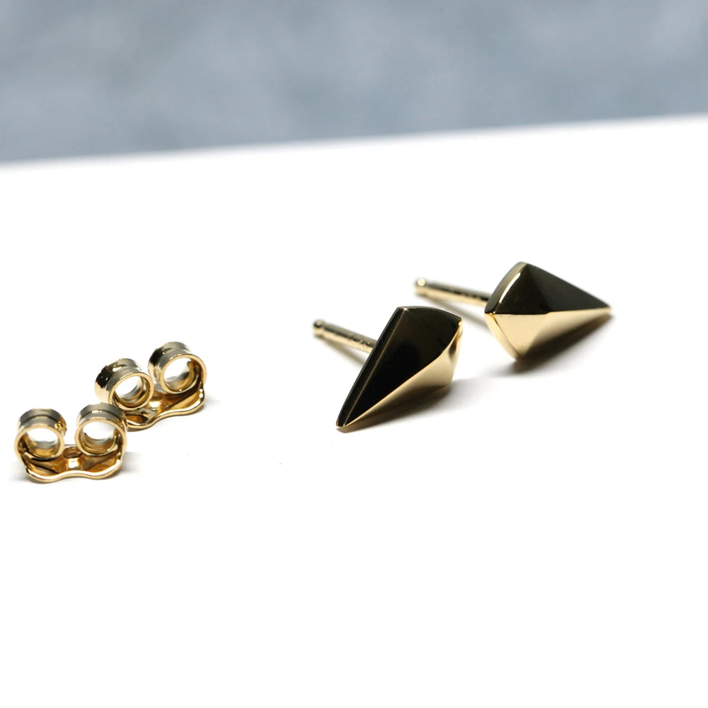 Sculptural gold earrings displayed on textured beige stone, showcasing bold lines and contrasting metal tones.